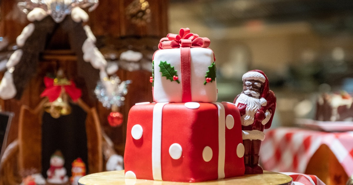 A two-tiered Christmas cake. Each tier is decorated like a present with red and white ribbons, polka dots, and holly leaves.