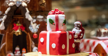 A two-tiered Christmas cake. Each tier is decorated like a present with red and white ribbons, polka dots, and holly leaves.