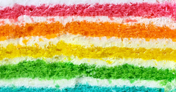 A layered cake where each layer is a different color of the rainbow. There is white frosting between each layer.